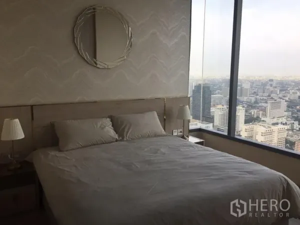Condominium for rent in Watthana, Bangkok - Master bedroom with panoramic city skyline through floor‑to‑ceiling window and neutral decor.