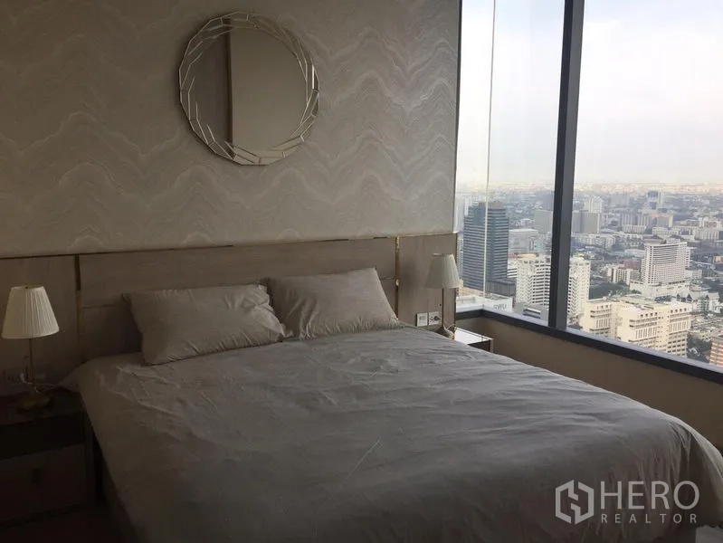 Condominium for rent in Watthana, Bangkok - Master bedroom with panoramic city skyline through floor‑to‑ceiling window and neutral decor.