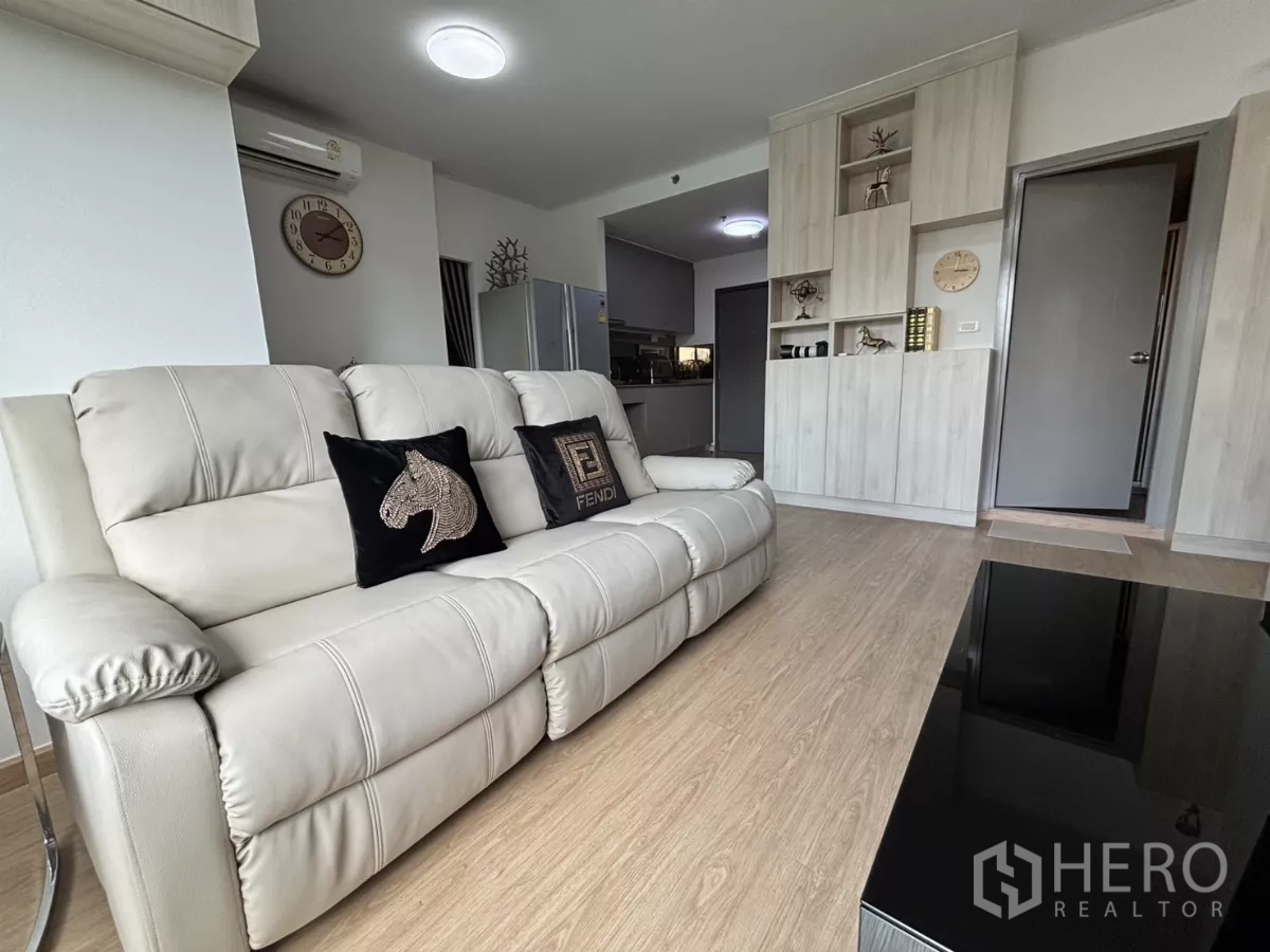 Condominium for rent in Phra Khanong, Bangkok - Bang Chak condo living room with cream leather sofa, built-in cabinetry and wood floors leading to the kitchen.