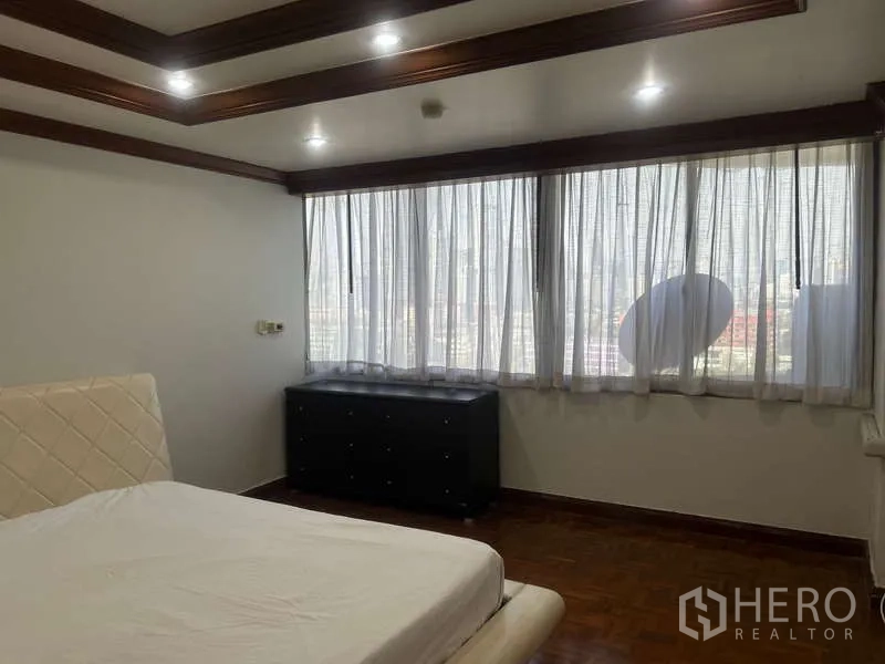 Condominium for sale in Huai Khwang, Bangkok - Bedroom with large window and city outlook filtered by sheer curtains, plus dark dresser.