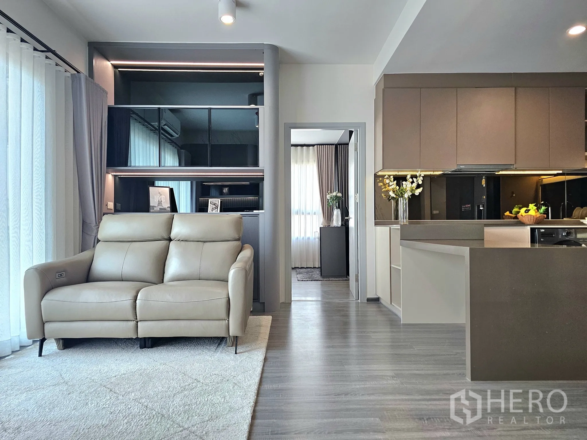 公寓 for sale in Bang Rak, Bangkok - 客厅一角的皮质双人沙发、展示层架以及通往卧室的门。