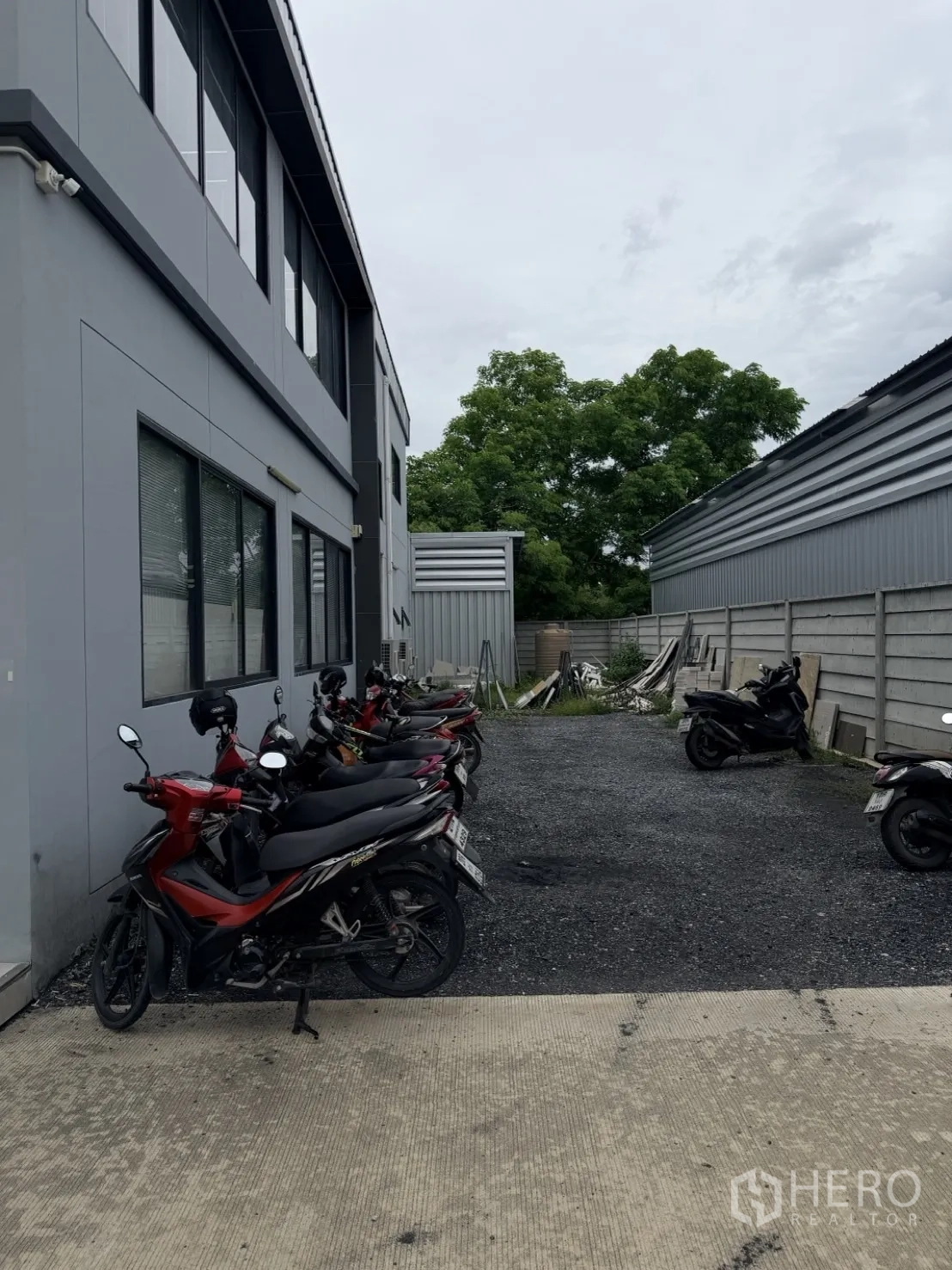 โรงงาน for rent or sale in Lam Luk Ka, Pathum Thani - ทางเดินด้านนอกอาคารสำนักงานสีเทาพร้อมที่จอดมอเตอร์ไซค์.