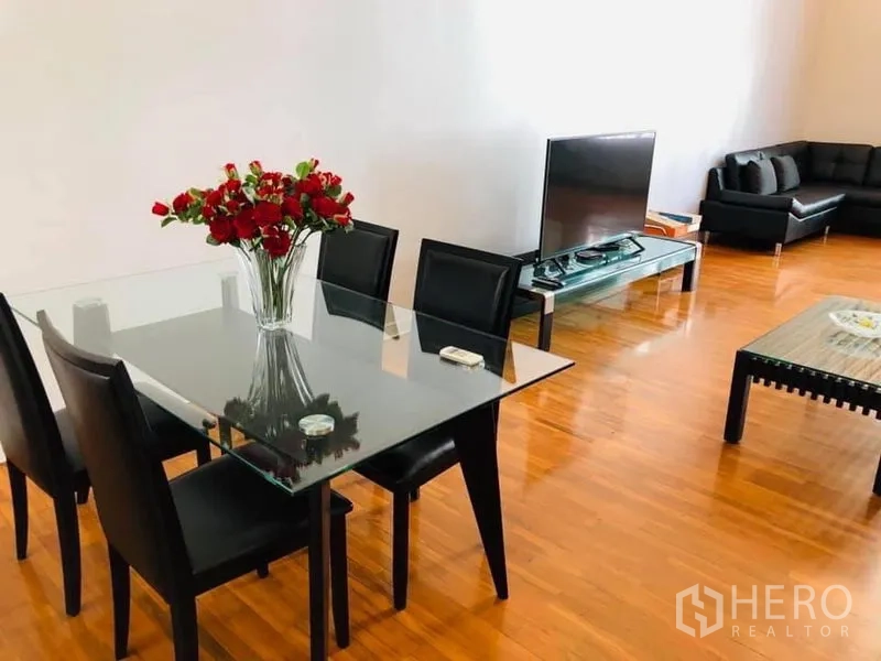 Townhouse for rent in Khlong Toei, Bangkok - Open-plan dining area with glass table, TV stand and black leather sofas.