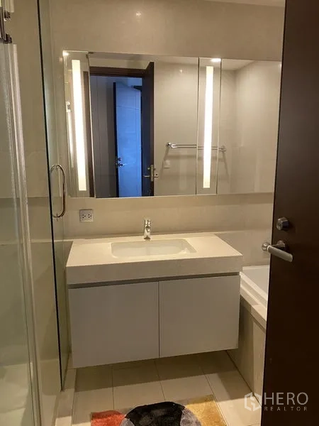 公寓 出租在Watthana, Bangkok - 现代浴室，带灯镜柜、白色洗手台与局部浴缸，米色瓷砖。