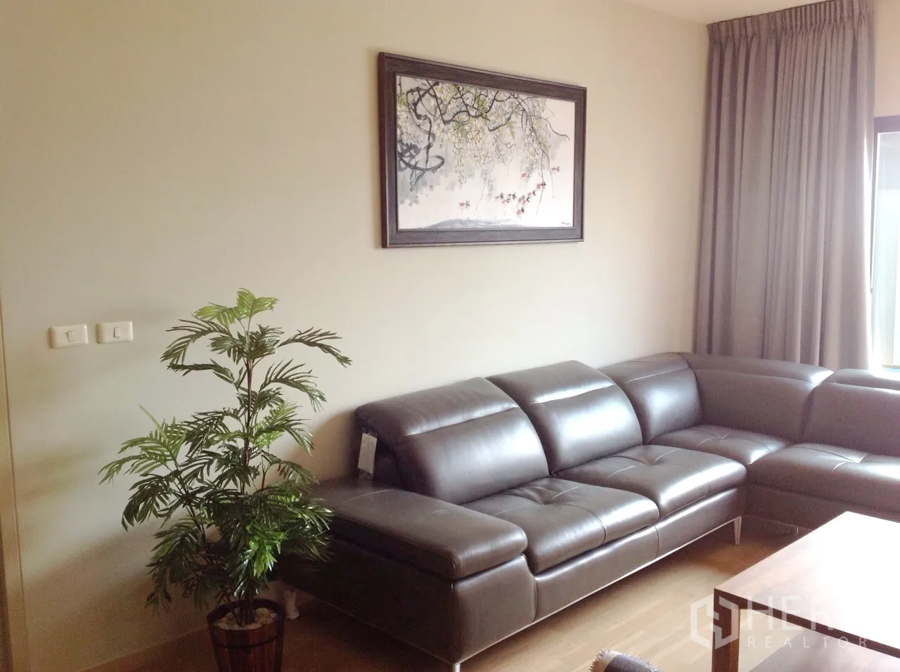 Condominium for rent or sale in Watthana, Bangkok - Bright living room with an L-shaped leather sofa, wall art and a potted plant.