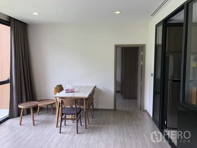 Condominium for rent in Watthana, Bangkok - Bright dining area with a wooden table and chairs beside a full-height window and curtains.