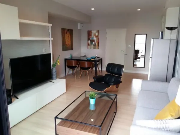 Condominium for rent in Sathon, Bangkok - Bright living-dining area with TV console, Eames-style lounge chair, four-seat dining set and wall art.
