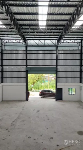 货栈 出租在Khlong Toei, Bangkok - 室内视角，可见高挑钢结构屋架与入口卷帘门。