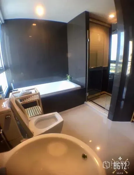 Condominium for rent in Sathon, Bangkok - Modern bathroom featuring bathtub, separate glass shower, toilet and basin with dark wall tiles and window light.