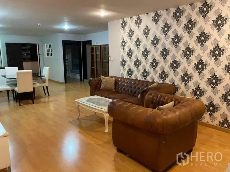 Condominium for rent or sale in Watthana, Bangkok - Open-plan living area with brown leather sofas, patterned feature wall, and wood flooring in a Bangkok condo.