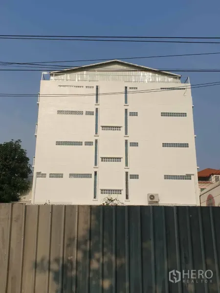 Office Space for rent or sale - Rear elevation of a tall white commercial building behind a metal fence.