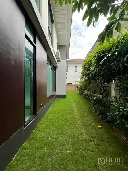 Detached House for rent in Bang Kapi, Bangkok - Side lawn with trimmed hedges along exterior windows of the house.