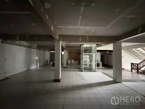 办公空间 出租在Watthana, Bangkok - 一层开放式空间，瓷砖地面，立柱与玻璃电梯井。