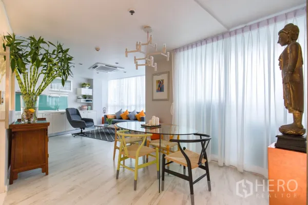 公寓 出租在Pathum Wan, Bangkok - 从餐区望向客厅和一体化厨房，白色橱柜、绿色玻璃背板与现代吊灯。