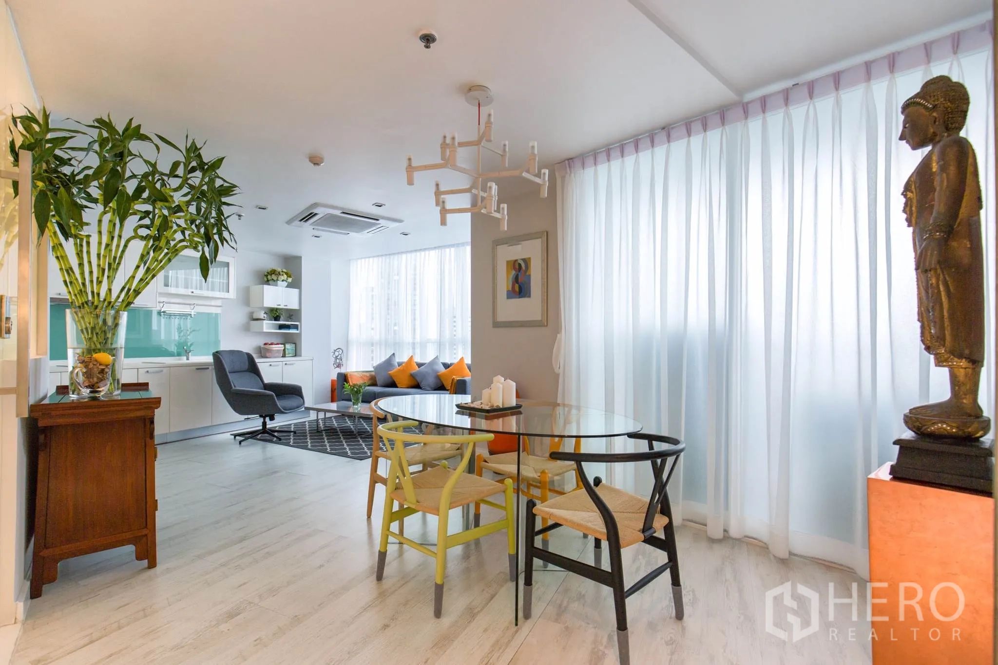 公寓 出租在Pathum Wan, Bangkok - 从餐区望向客厅和一体化厨房，白色橱柜、绿色玻璃背板与现代吊灯。