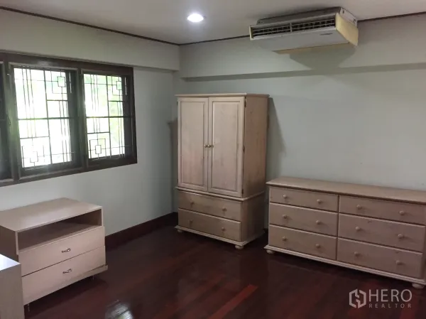 Detached House for rent in Khlong Toei, Bangkok - Bedroom with polished wooden floors, window grilles and light wood dressers.