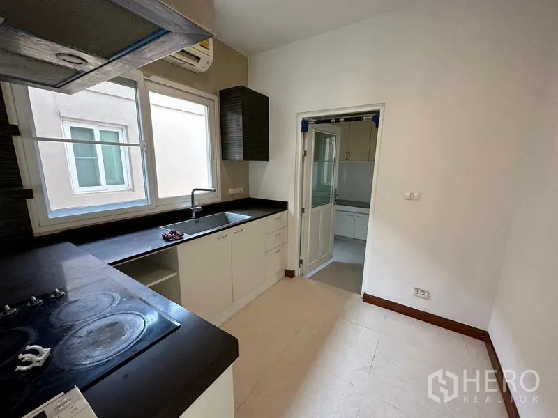 Detached House for rent or sale in Pak Kret, Nonthaburi - Western kitchen with black countertops and window, connected to Thai kitchen.