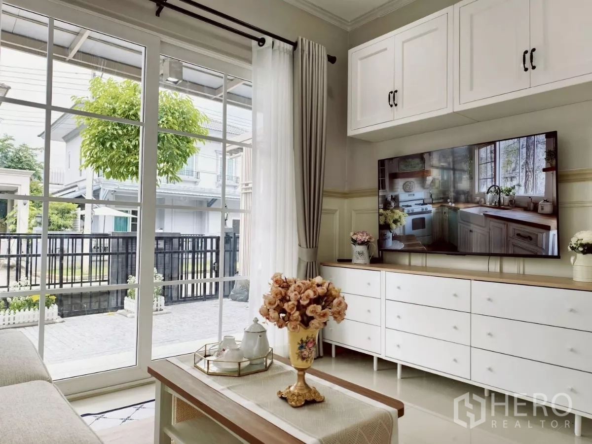 独立式住宅 出租在Khlong Luang, Pathum Thani - 客厅带电视柜与茶几，对望落地玻璃门与庭院