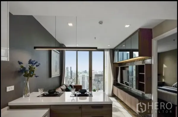 Condominium for rent in Bang Rak, Bangkok - Open-plan kitchen and living room with island, TV wall and floor-to-ceiling windows overlooking Bangkok skyline.