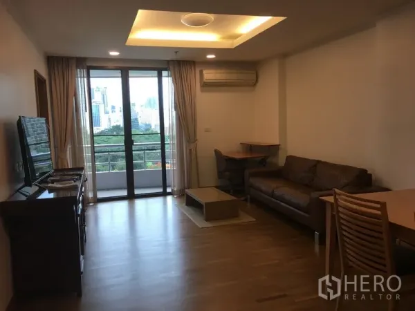 คอนโด ให้เช่าในPathum Wan, Bangkok - ห้องนั่งเล่นหันออกสู่ระเบียง เปิดรับวิวสกายไลน์และพื้นที่สีเขียว พร้อมโซฟาสีน้ำตาลและพื้นไม้