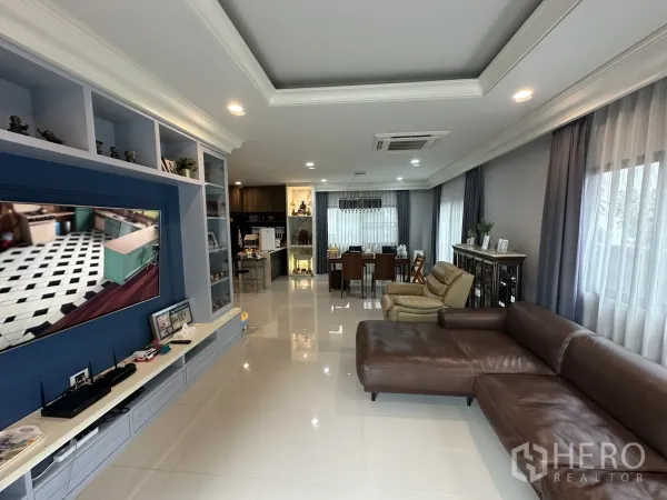 บ้าน ให้เช่าในLam Luk Ka, Pathum Thani - พื้นที่นั่งเล่นยาว มีผนังทีวี โซฟา และโซนทานอาหารริมหน้าต่าง