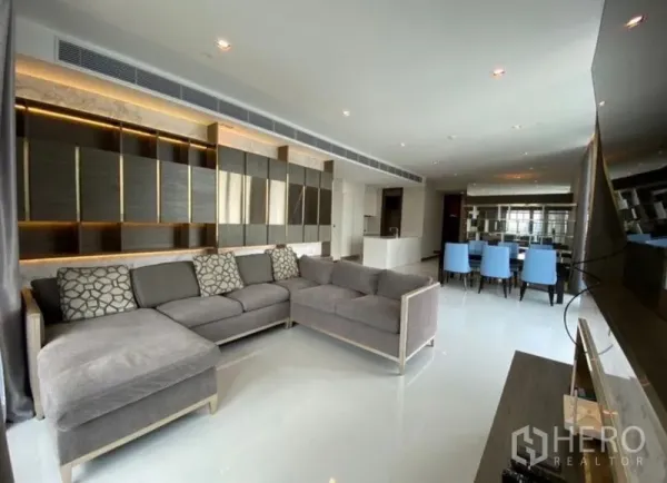 公寓 出租在Khlong Toei, Bangkok - 开放式客餐厅，L 形沙发、蓝色餐椅与现代装饰墙。