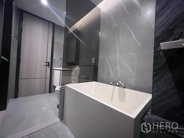 คอนโด ให้เช่าในKhlong Toei, Bangkok - ภาพระยะใกล้ของอ่างอาบน้ำลึกข้างผนังลายหินในห้องน้ำร่วมสมัย