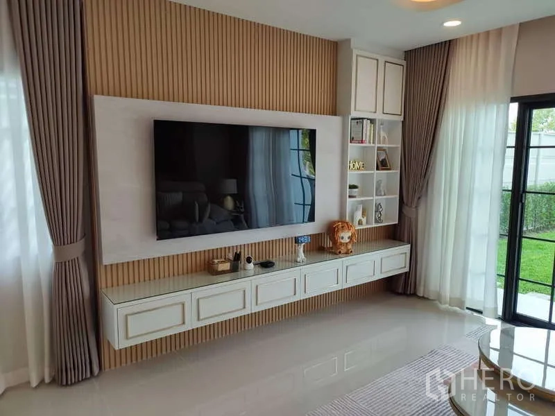 Detached House for rent in Bang Phli, Samut Prakan - Living room feature wall with large mounted TV, floating cabinet and garden view.