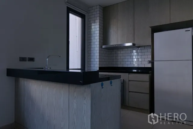 联排别墅 出租在Watthana, Bangkok - 现代厨房，地铁砖挡板、黑色台面与不锈钢冰箱。