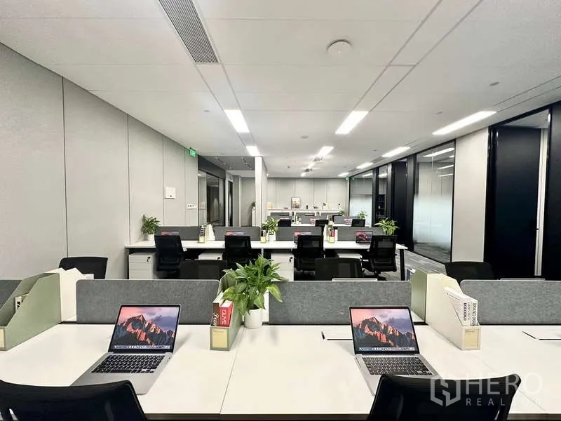 สำนักงาน ให้เช่าในBang Kapi, Bangkok - สำนักงานแบบเปิดโล่ง โต๊ะทำงานเรียงเป็นแถว พร้อมโน้ตบุ๊กและกระถางต้นไม้ ใต้ไฟ LED