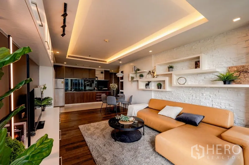 公寓 出售在Khlong Toei, Bangkok - 客厅另一视角，白色砖墙与悬浮层架，长条沙发、餐桌和开放式厨房。