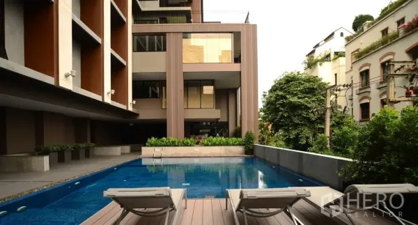 公寓 出租或出售在Sathon, Bangkok - 沙吞现代公寓的庭院泳池区，设有日光躺椅与绿化景观。