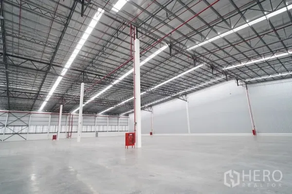 Warehouse for rent in Khlong Luang, Pathum Thani - High-ceiling storage hall featuring tall columns, fire safety systems, and bright linear lighting.