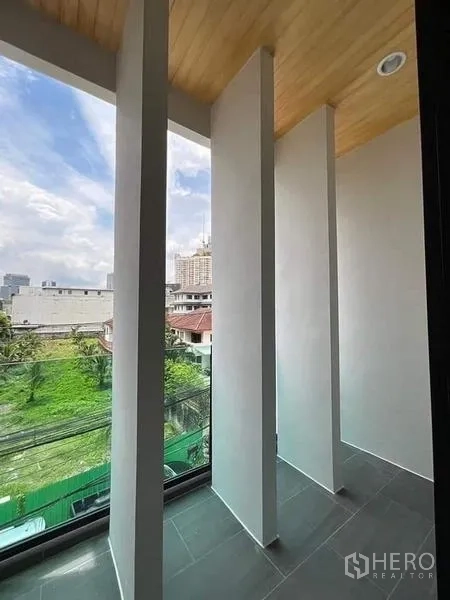Townhouse for sale in Watthana, Bangkok - Slim balcony with vertical fins and glass railing overlooking neighborhood greenery.