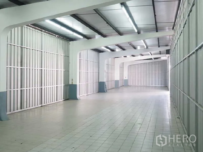 Warehouse for rent in Bang Kapi, Bangkok - Tall warehouse aisle with metal cladding walls, tiled floor and strip lighting along the ceiling.