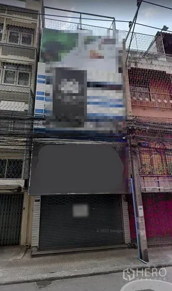 อาคารพาณิชย์ ให้เช่าในKhlong Toei, Bangkok - ด้านหน้าอาคารพาณิชย์หลายชั้นริมถนนแคบในกรุงเทพฯ พร้อมประตูม้วน ป้ายหน้าร้านโล่ง และสายสื่อสารพาดผ่าน