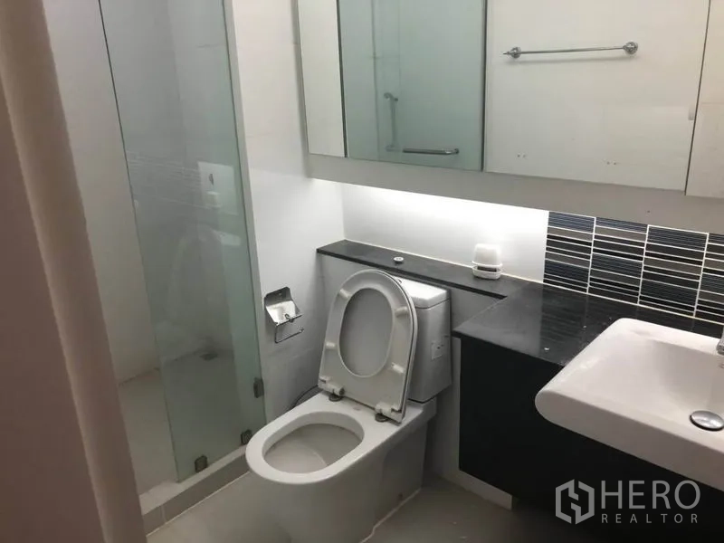 Condominium for sale in Bang Na, Bangkok - Contemporary bathroom with glass-enclosed shower, mirrored cabinet, vanity and toilet.