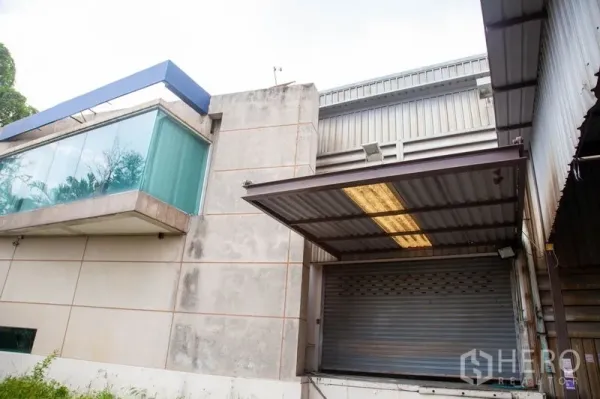 货栈 出租在Prawet, Bangkok - 装卸区带卷闸门与雨棚，旁有悬挑玻璃角落办公室。