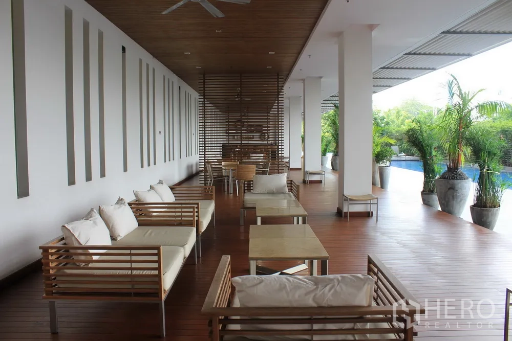 Condominium for rent or sale in Yan Nawa, Bangkok - Covered poolside lounge with wooden deck, sofa seating and tropical planters.