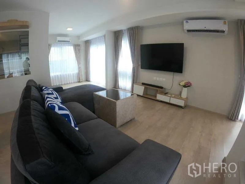 Townhouse for rent - Living area with dark sectional sofa, TV console, and wide glazed doors.
