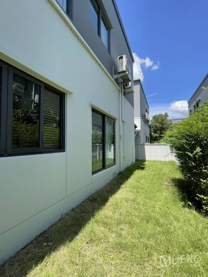Detached House for rent in Bang Phli, Samut Prakan - Lawned side yard running along the house facade under blue sky.