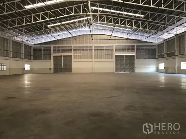 工厂 出租在Mueang Samut Prakan, Samut Prakan - 大型厂房内部，高钢结构桁架屋顶，抛光混凝土地面与双扇推拉钢门。