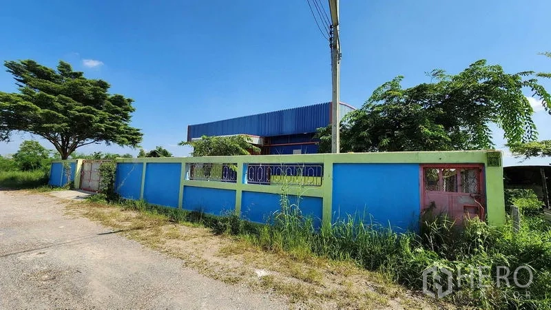 货栈 出租在Nong Chok, Bangkok - 街景可见蓝色围墙与绿树，环绕曼谷农乔区的低层仓库。