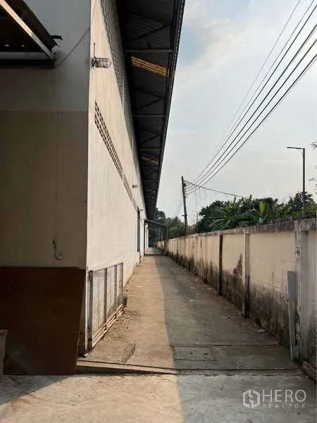 货栈 出售在Bang Bua Thong, Nonthaburi - 仓库侧边狭长混凝土人行道，沿围墙与管线而行。