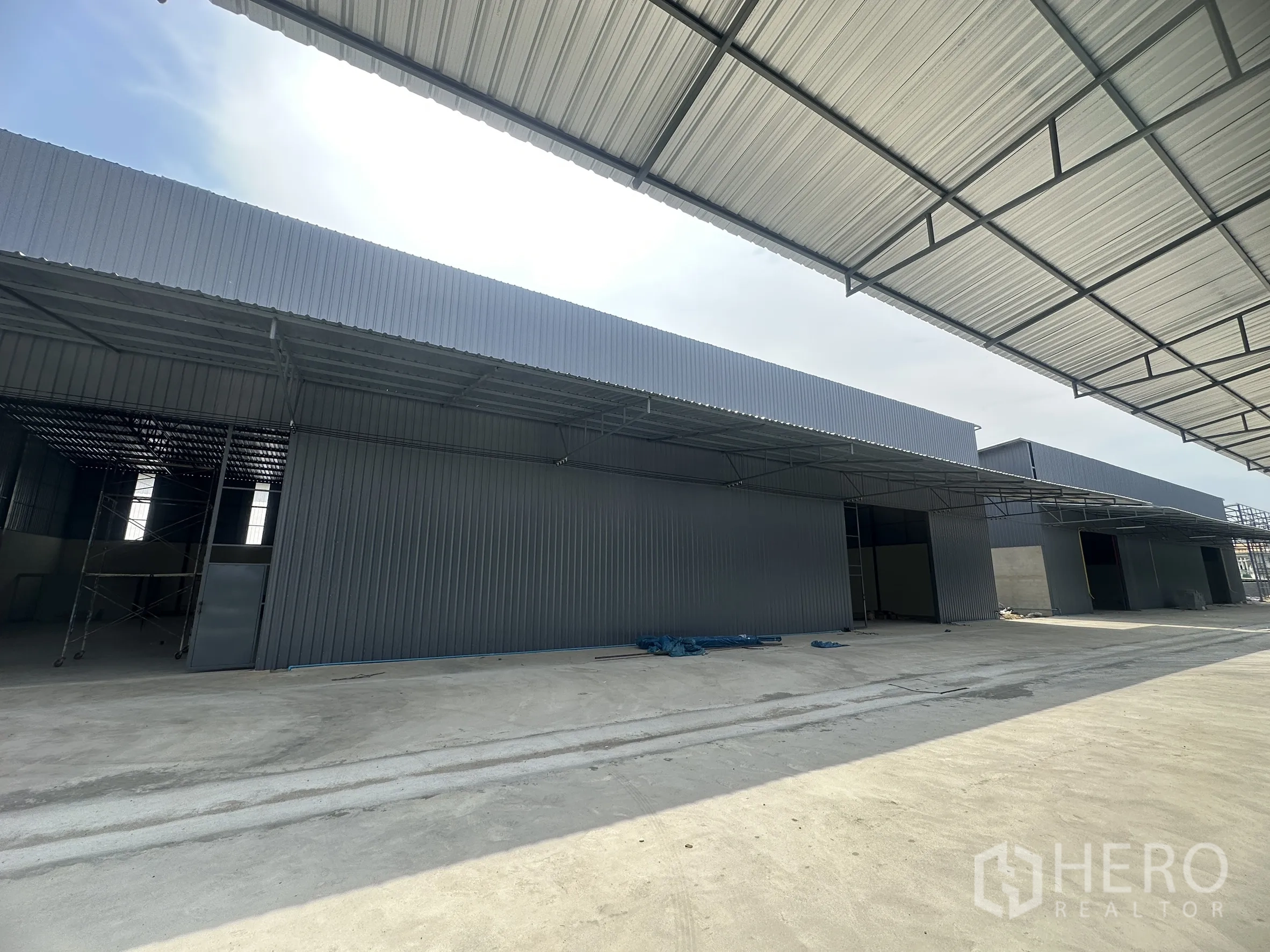 Warehouse for rent in Lam Luk Ka, Pathum Thani - Row of warehouse units with metal cladding and covered loading bays along a paved drive.