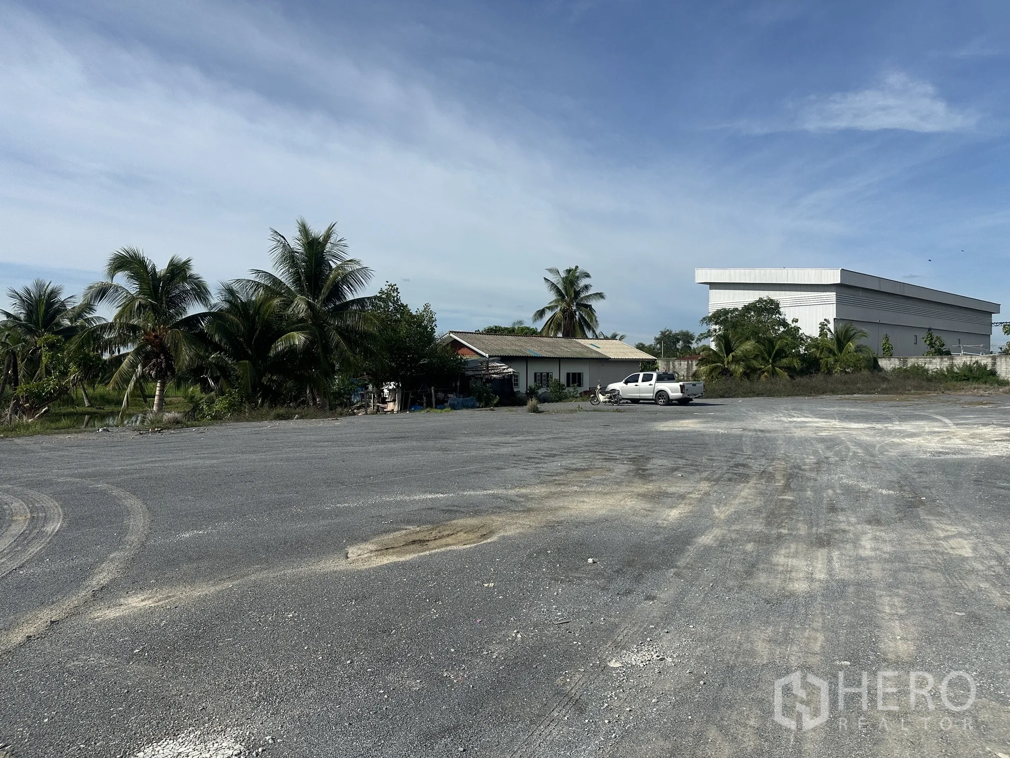 Land for sale in Sai Noi, Nonthaburi - Open prepared site with palm trees, a small house and a parked pickup beside a warehouse.