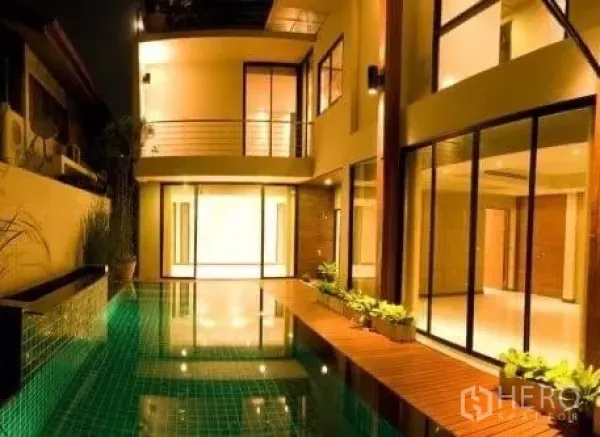 Detached House for rent in Khlong Toei, Bangkok - Private pool courtyard beside glass‑walled living areas illuminated at night.