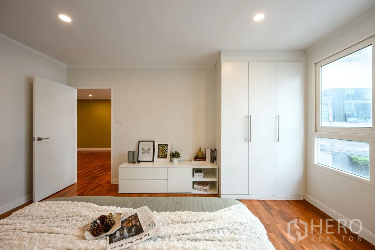 Condominium for sale in Watthana, Bangkok - Bedroom storage area with built-in white wardrobe, low cabinet, and corner windows.