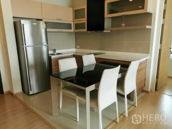 Condominium for rent in Khlong Toei, Bangkok - Modern kitchen with stainless refrigerator, built-in cabinetry, induction cooktop and black glass dining table for four.