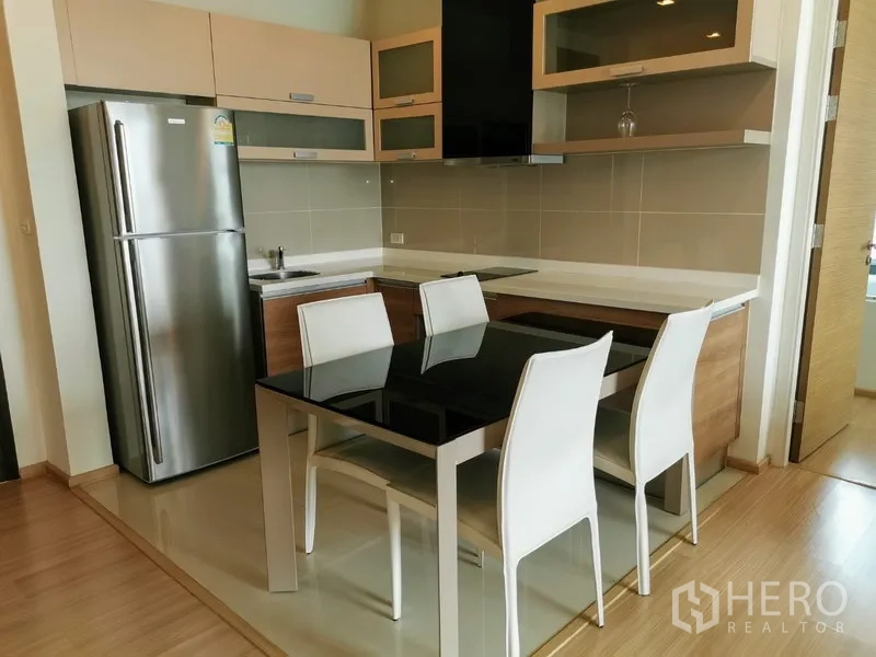 Condominium for rent in Khlong Toei, Bangkok - Modern kitchen with stainless refrigerator, built-in cabinetry, induction cooktop and black glass dining table for four.
